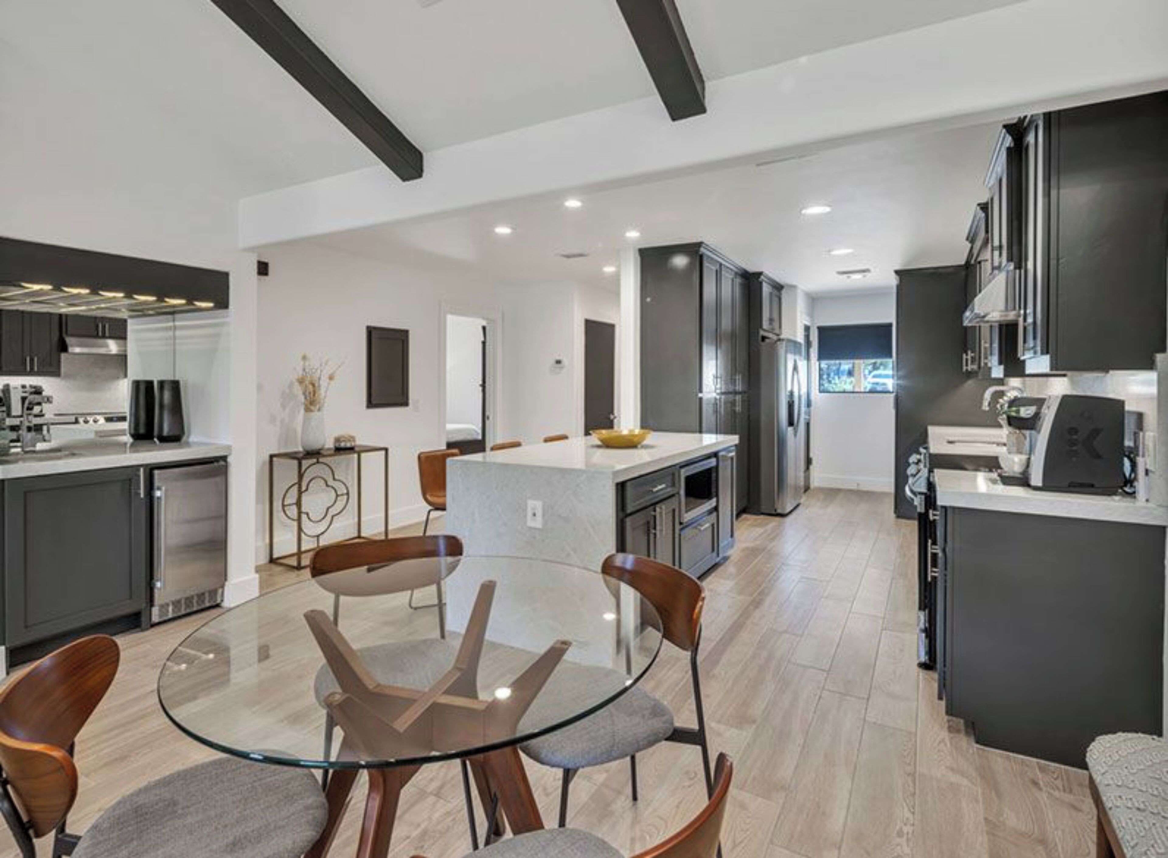 Una cocina moderna con una isla central, muebles oscuros y una mesa de vidrio con sillas.