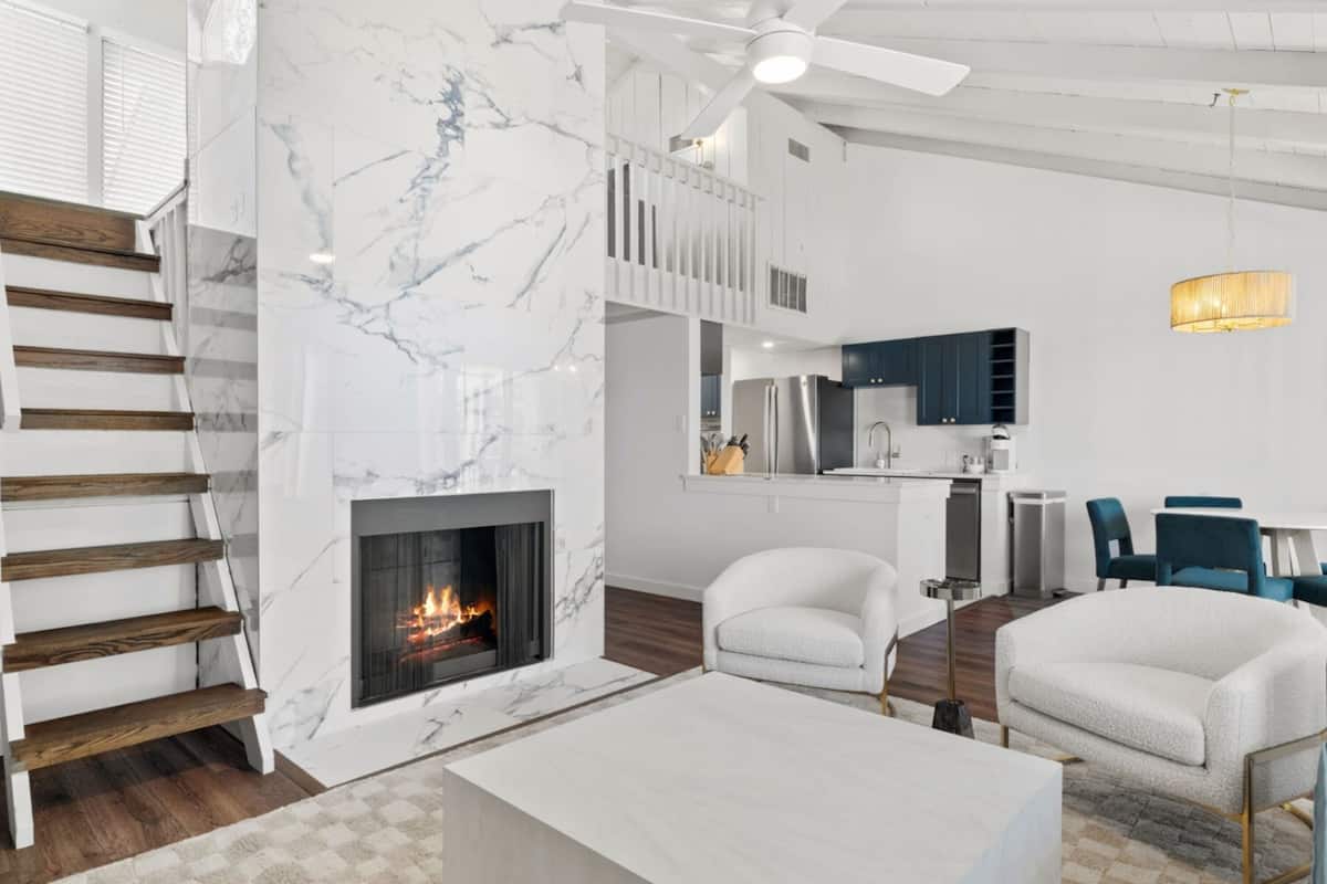 A modern living room with a fireplace, white furniture, and a staircase.