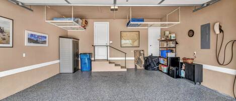 A garage with a concrete floor, a staircase, a refrigerator, and a blue trash bin.