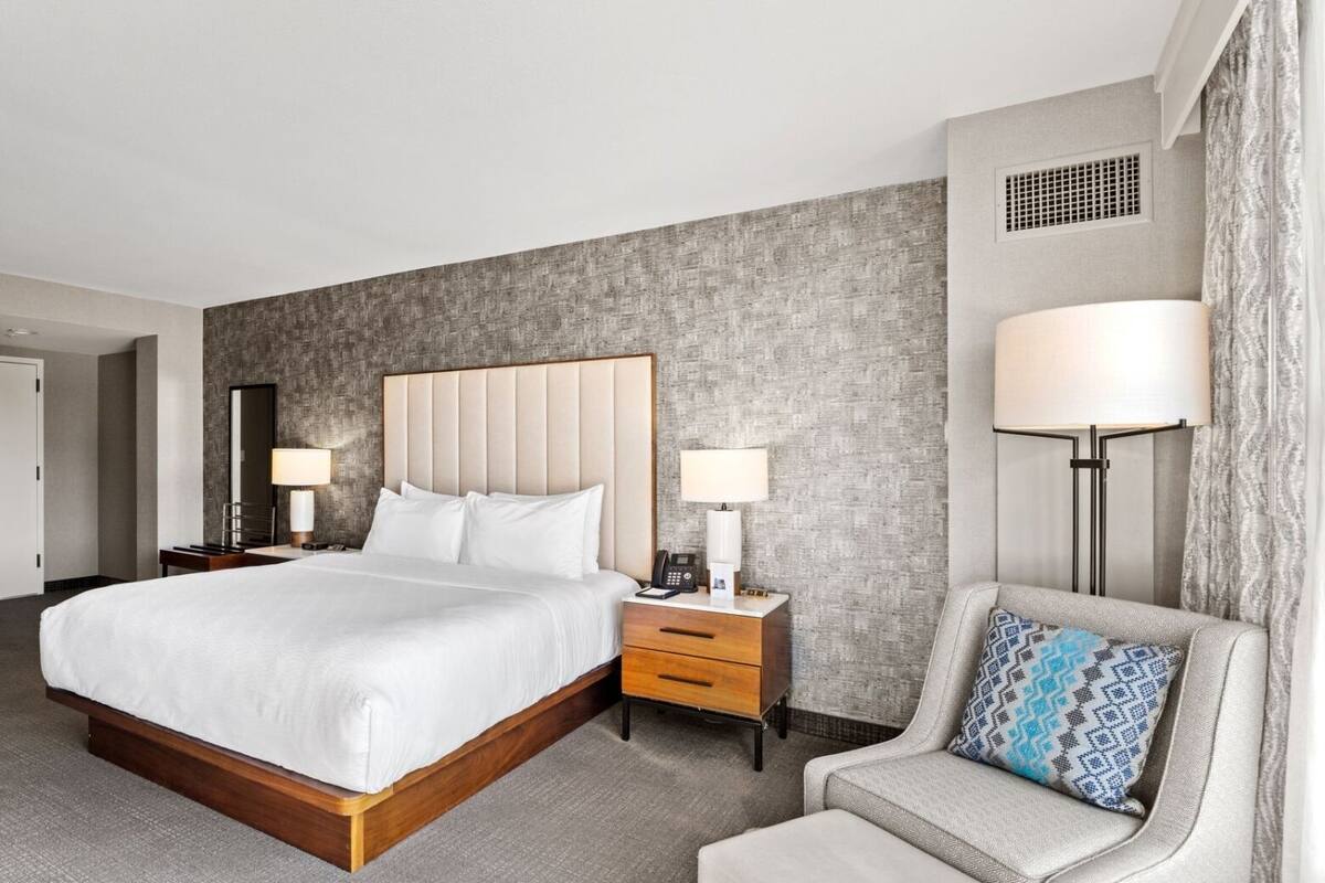 A hotel room with a large bed, bedside tables, a chair, and a lamp.