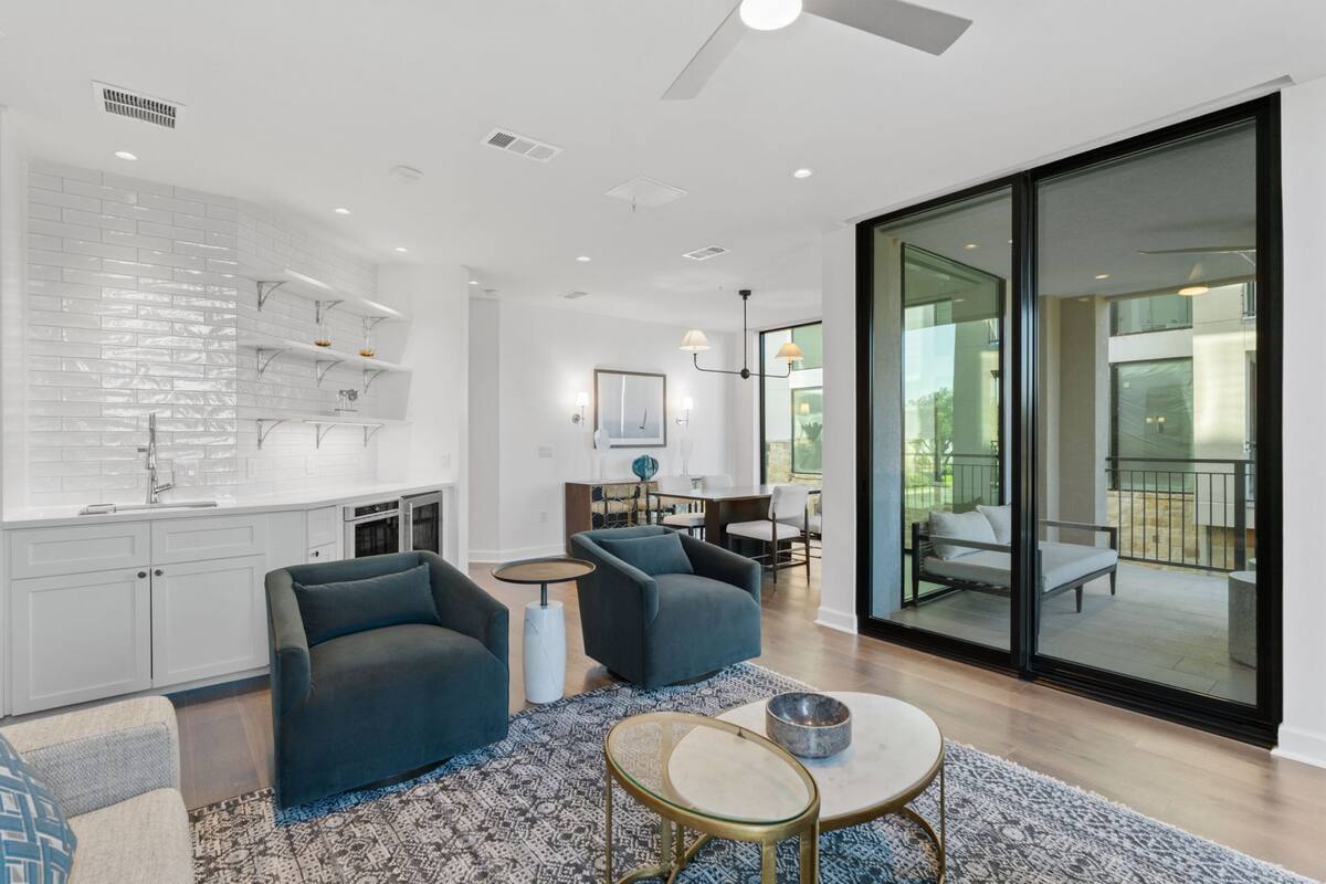 A modern kitchen with white cabinets and a brick backsplash, a dining area with a table and chairs, and a large sliding glass door leading to an outdoor patio.