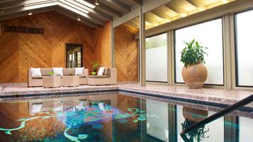 A modern indoor pool area with a wooden wall and a sofa by the pool.