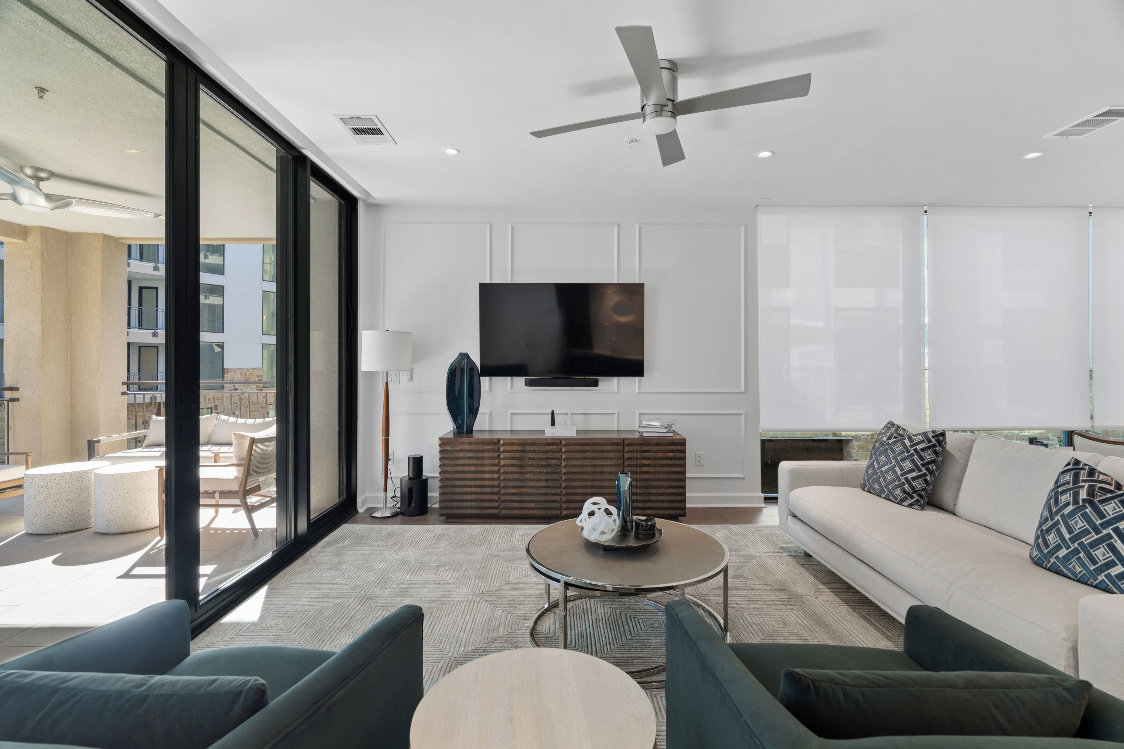 Uma sala de estar moderna com televisão de tela plana, ventilador de teto e uma grande janela.