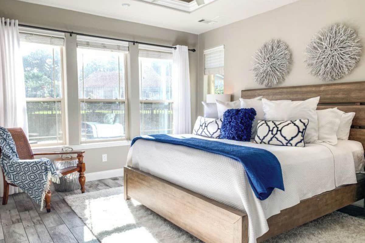 A bedroom with a large bed, a chair, and a view of the outside through large windows.