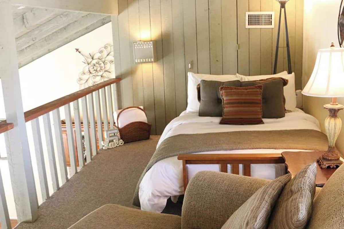 A bedroom with a bed, a nightstand, a lamp, a chair, and a decorative wall piece.