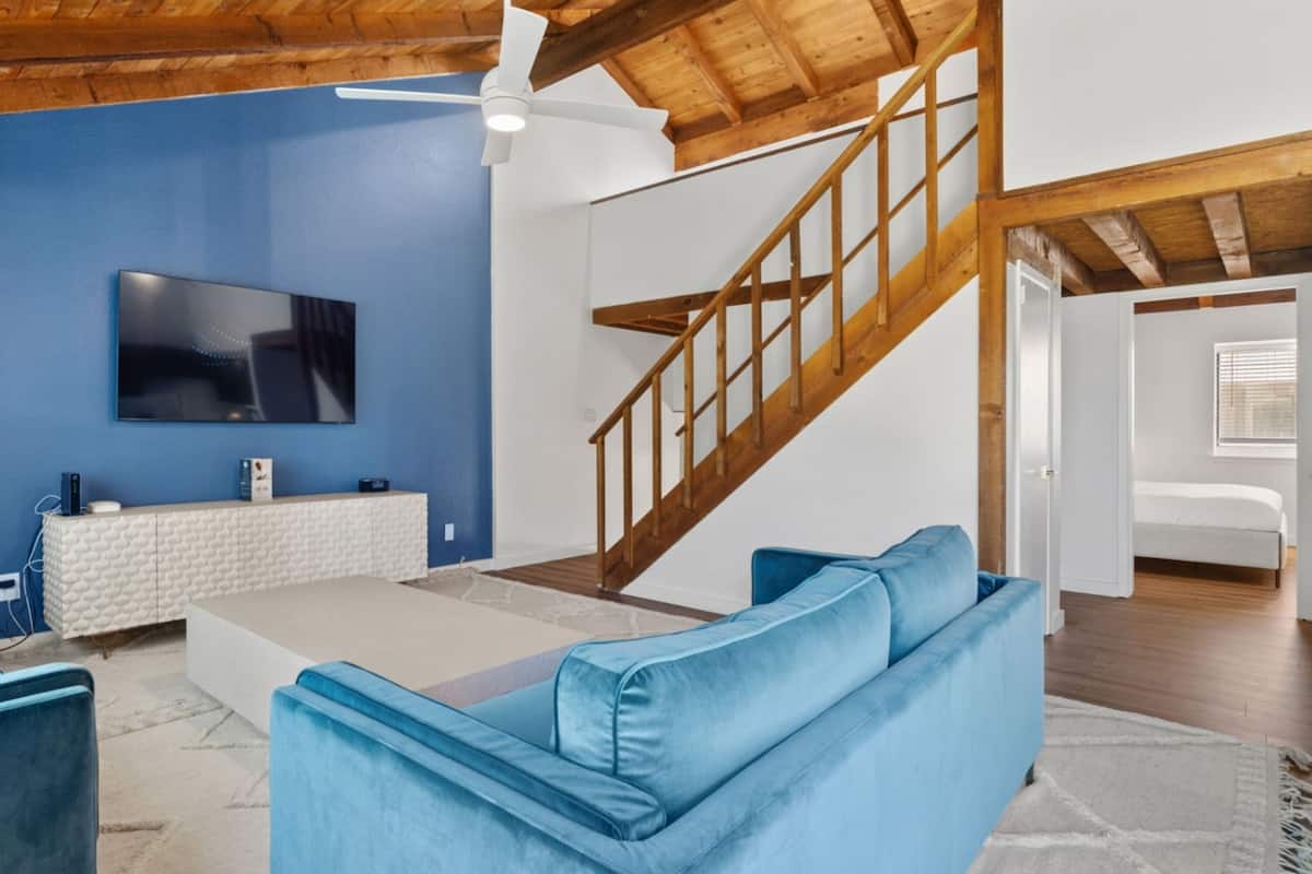 A modern living room with a blue wall, a white entertainment unit, a blue sofa, and a wooden staircase.