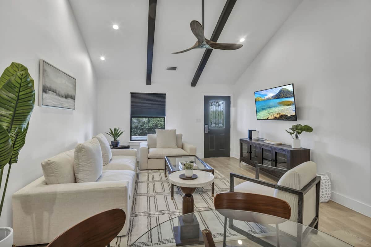 A spacious living room with a high ceiling, a ceiling fan, a large window, a sofa, a coffee table, and a TV.