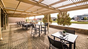 Un espace extérieur aménagé en terrasse, avec un sol en briques, des tables, des chaises et une structure en forme de pergola.