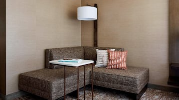 A corner seating area with a brown upholstered sofa, a small white side table, a patterned cushion, and a white lamp.