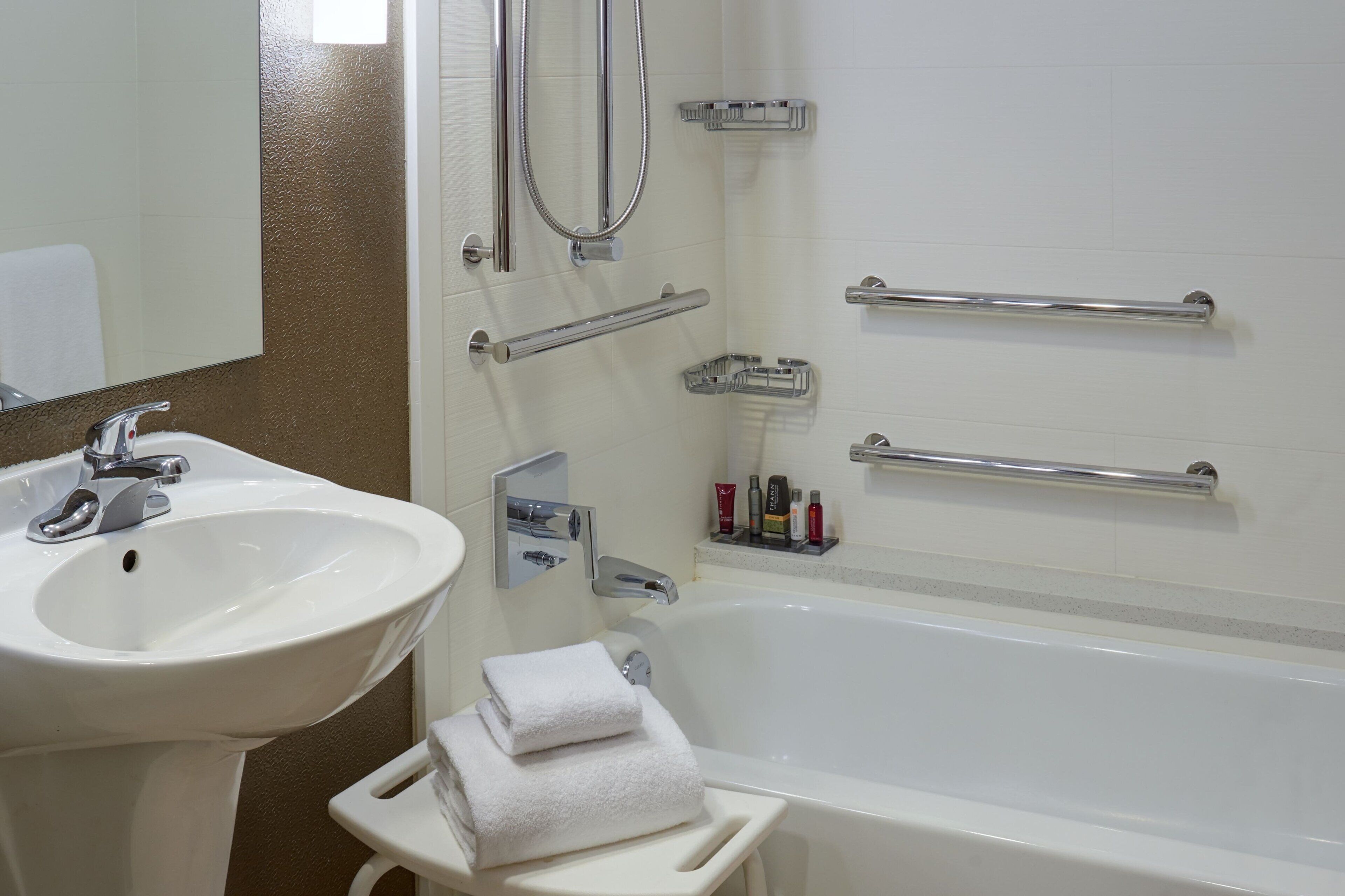 A bathroom with a white sink, a bathtub, and a mirror. There are grab bars on the wall and a towel rack.