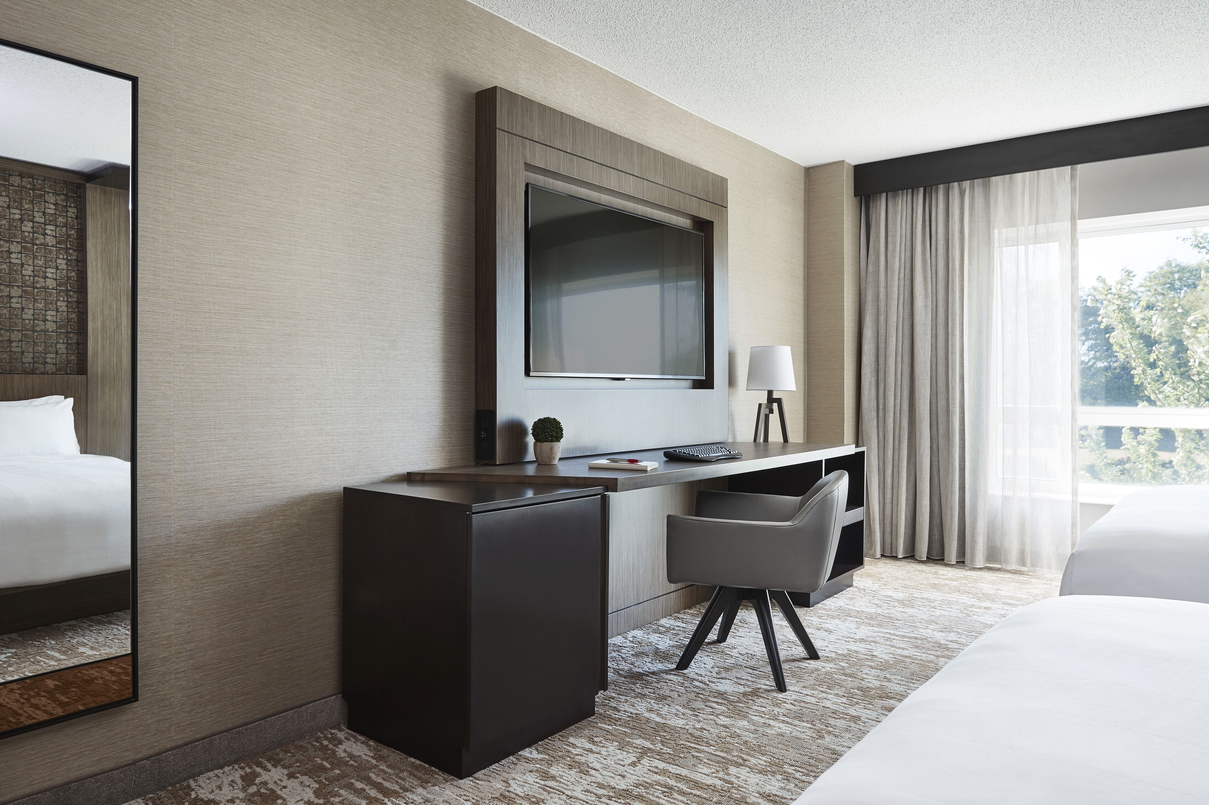 Une chambre d’hôtel moderne, dotée d’un grand lit, d’un bureau avec un ordinateur, d’une télévision et d’une fenêtre avec des rideaux.