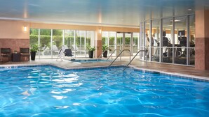 Une piscine intérieure à l’eau claire, entourée de chaises longues et d’appareils de musculation.
