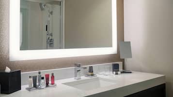 A modern bathroom with a large mirror, two sinks, and a shower.