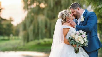 A couple embracing in a white wedding dress and blue suit, with a natural outdoor setting.