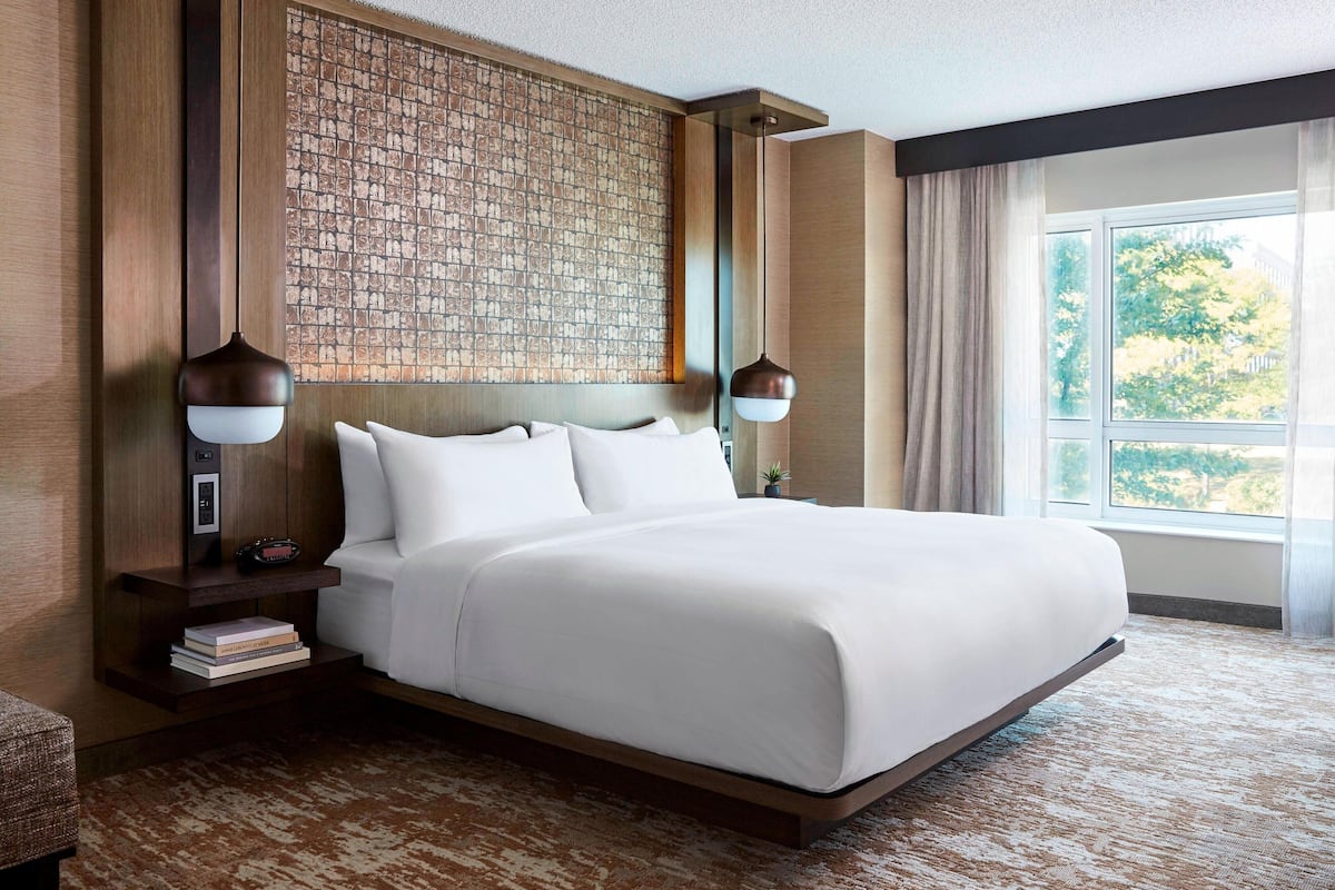 A large bed with white linens, a wooden headboard, and a textured wall behind it. There are two bedside tables with lamps and a small potted plant.