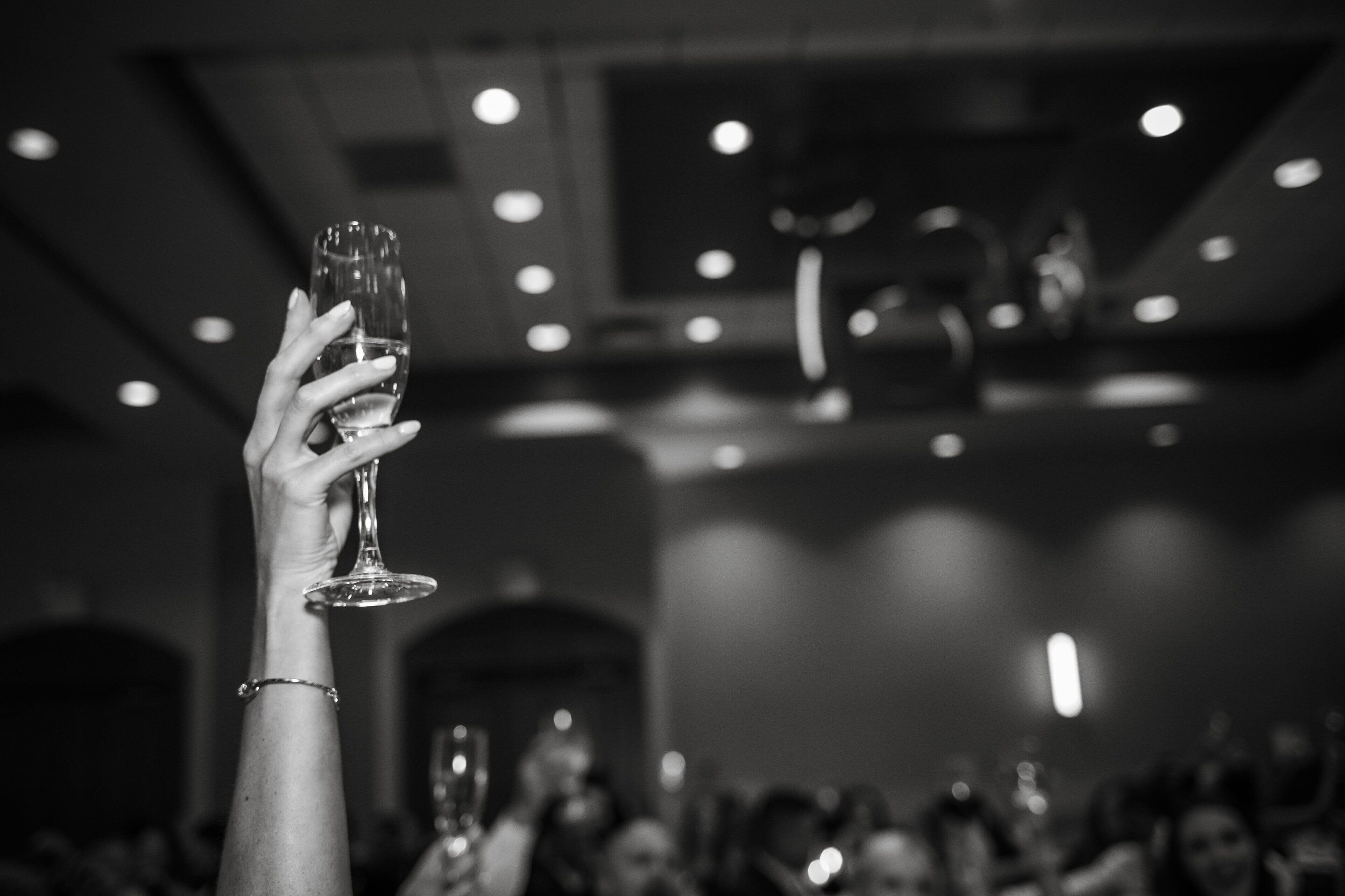 A hand holding a wine glass in a dimly lit room with a chandelier.