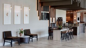 Un hall d’hôtel moderne comprenant un comptoir d’accueil, un bar et un espace détente avec des sièges.
