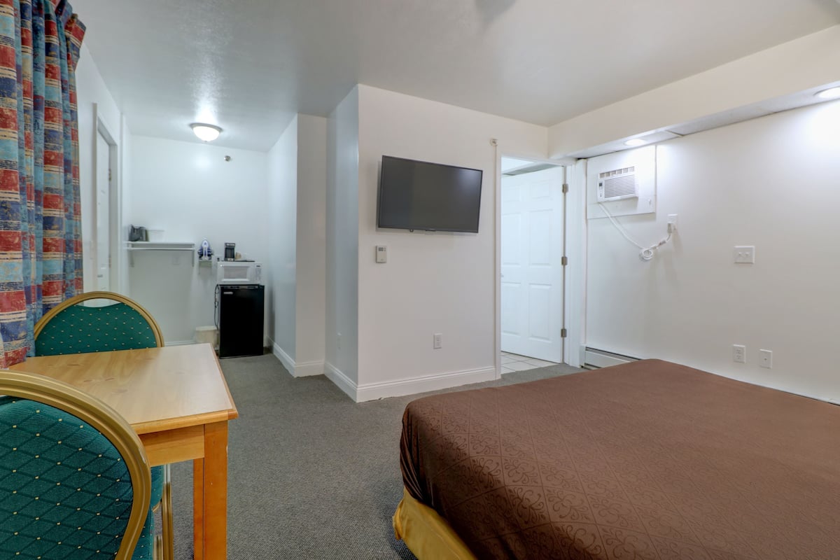 A hotel room with a bed, a TV mounted on the wall, a desk with a chair, and a wardrobe.