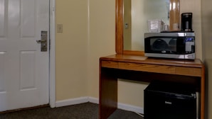 A hotel room with a wooden desk, a microwave, a coffee maker, and a black trash bin. - Classic Inn (Saco)