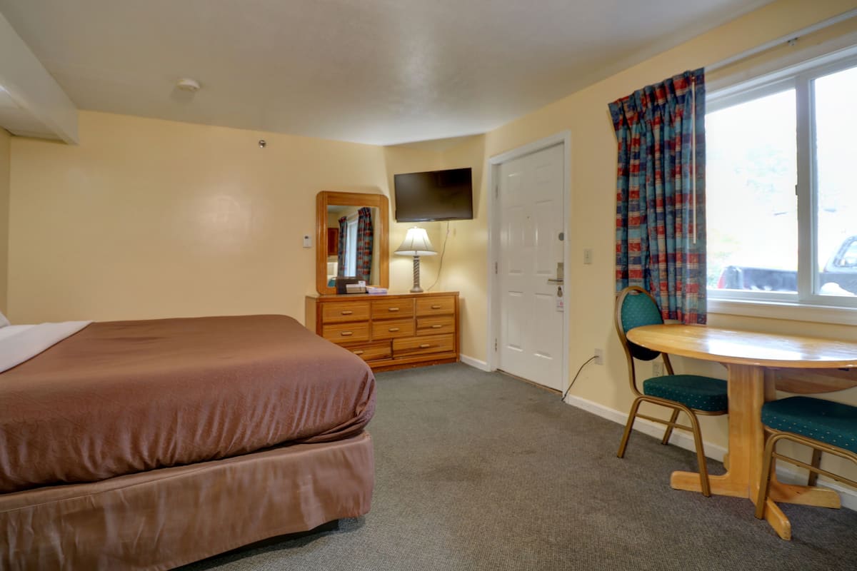 A hotel room with a bed, a dresser, a desk with a chair, a television, and a window with curtains.