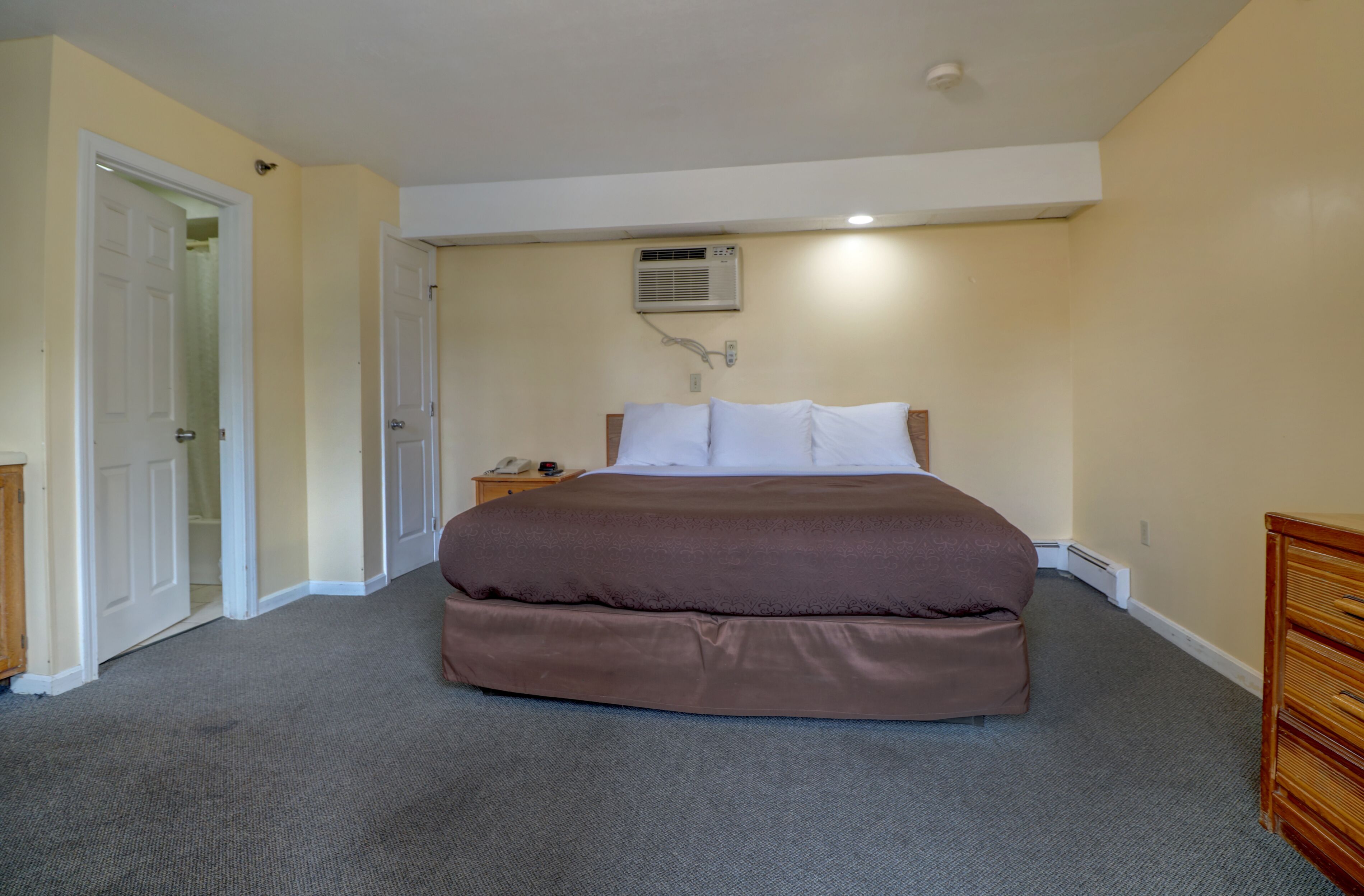 Slaapkamer met een groot bed, nachtkastje, een wandairco en een deur.