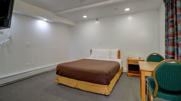 A hotel room with a bed, a desk with a chair, and a television on the wall.