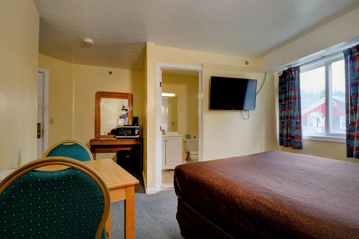 A hotel room with a bed, a desk with a chair, a television, and a window with curtains.