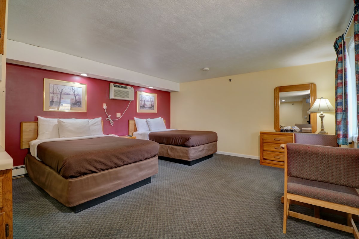 A hotel room with two beds, a desk, a chair, a dresser, a mirror, and two wall-mounted air conditioning units.