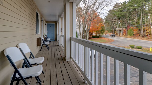 A wooden porch with white railings, a blue door, and two white folding chairs. - Classic Inn (Saco)