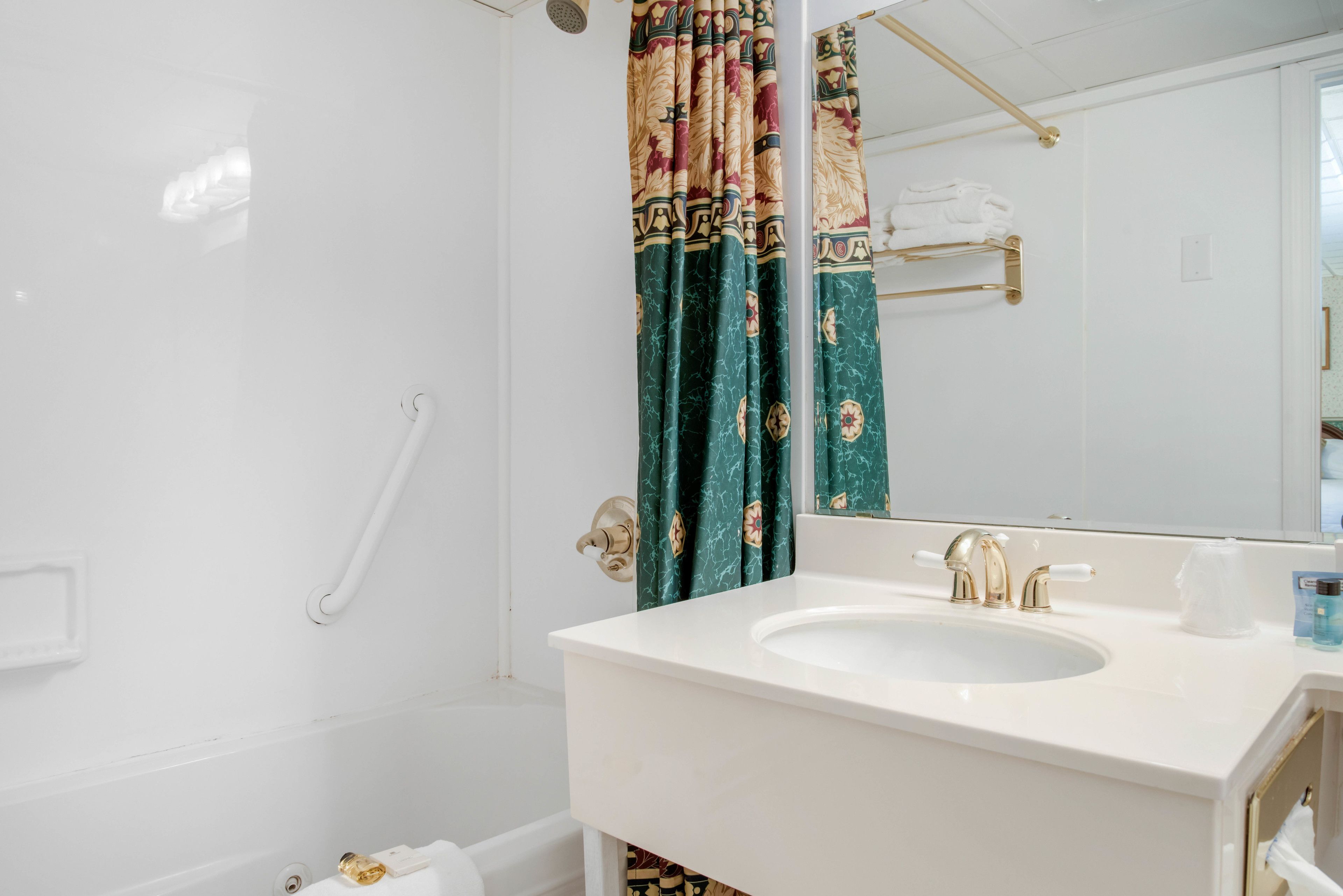 Een badkamer met een witte wastafel, gouden kraanwerk, een douchegordijn met bloemenprint en een handdoekhouder.
