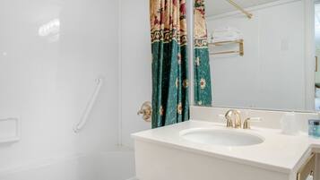 Een badkamer met een witte wastafel, gouden kraanwerk, een douchegordijn met bloemenprint en een handdoekhouder.