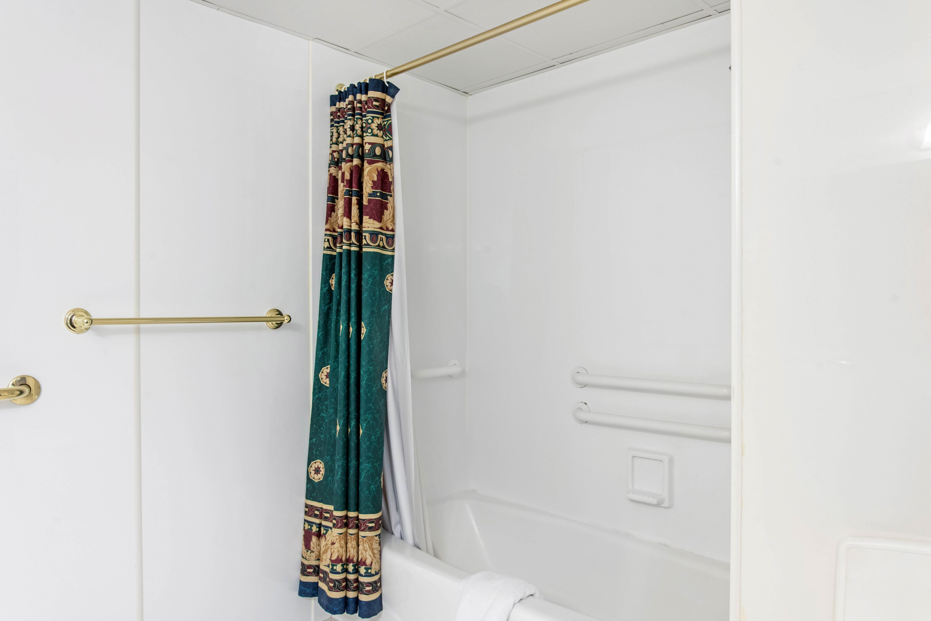 A bathroom with a white bathtub, a gold towel bar, and a patterned shower curtain.