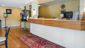 A reception area with a wooden counter, a coffee machine, a computer, and a clock on the wall. - Coachman Inn (Kittery)