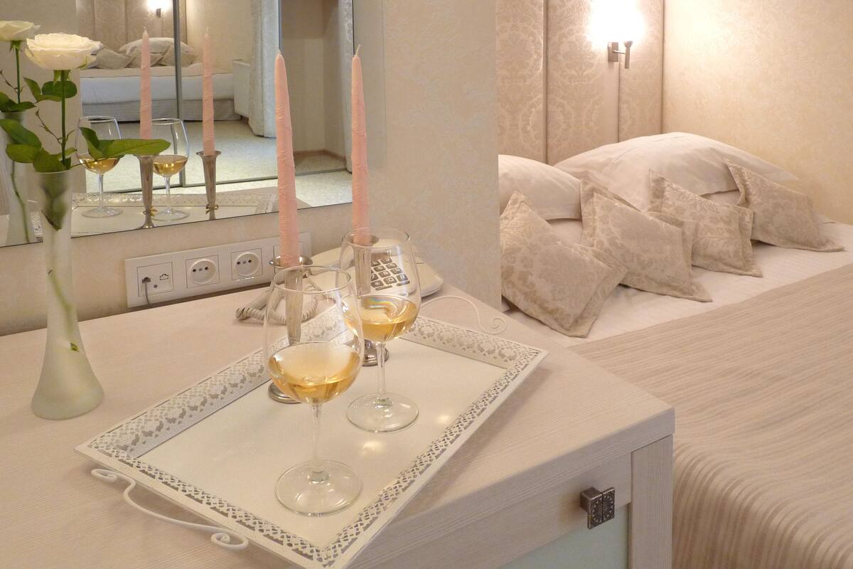 A bedroom with a bedside table holding a tray with two glasses of wine and three candles.
