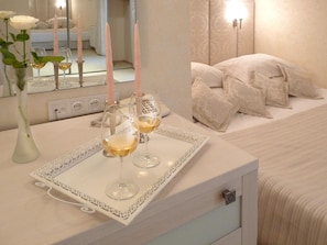 A bedroom with a bedside table holding a tray with two glasses of wine and three candles.