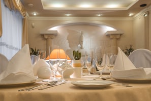 A dining table set with white napkins, plates, cutlery, and wine glasses, with a lamp and a cactus in a vase.