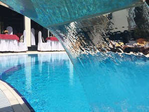 A swimming pool with clear blue water, a tiled deck, and white chairs with red covers. - Eney Hotel (Lviv)
