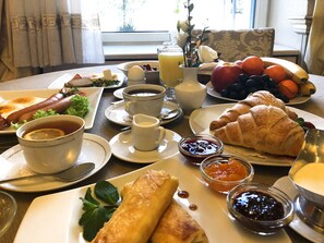 A breakfast table with various foods and drinks, including eggs, sausages, croissants, and fruit.