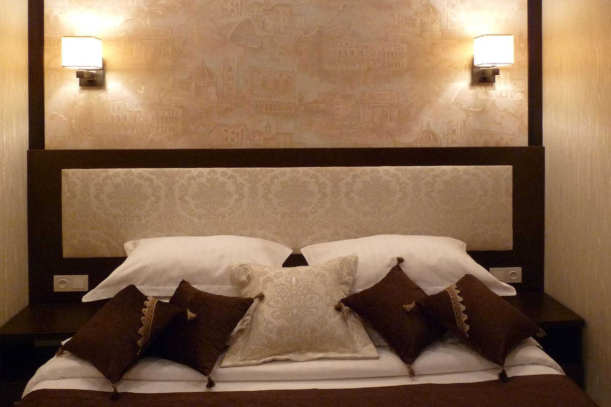 A neatly made bed with white and brown bedding, two nightstands with lamps, and a patterned wall behind the bed.