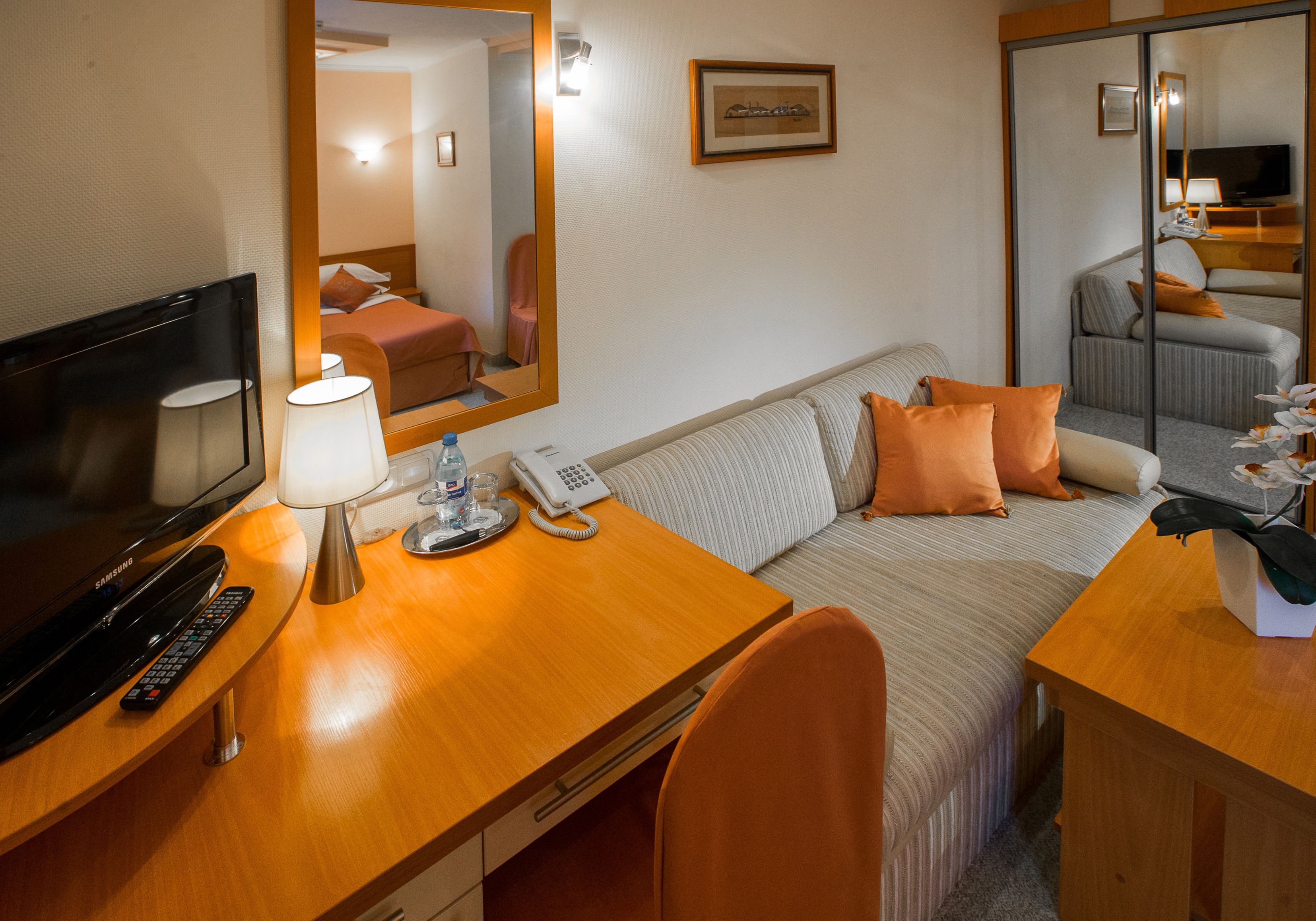 A hotel room with a bed, a desk with a lamp, a phone, a TV, and a mirror.