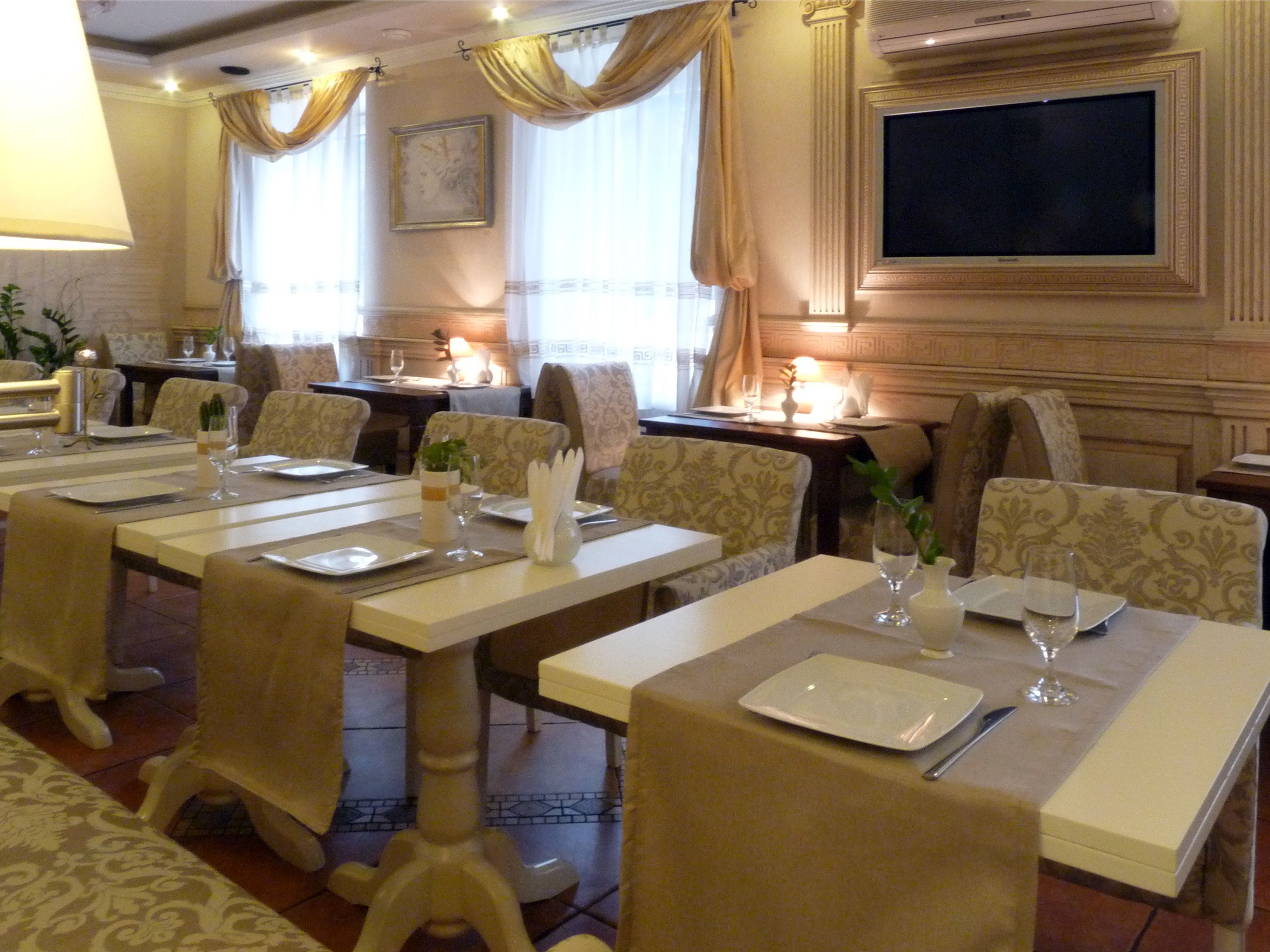 A dining area with multiple tables set for service, a television mounted on the wall, and a patterned wallpaper design.