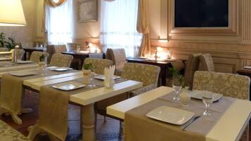 A dining area with multiple tables set for service, a television mounted on the wall, and a patterned wallpaper design.