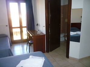 Una habitación de hotel con cama, escritorio, silla, inodoro y zona de ducha.