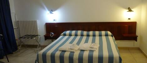 A hotel room with a large bed, two bedside lamps, a radiator, and a chair.