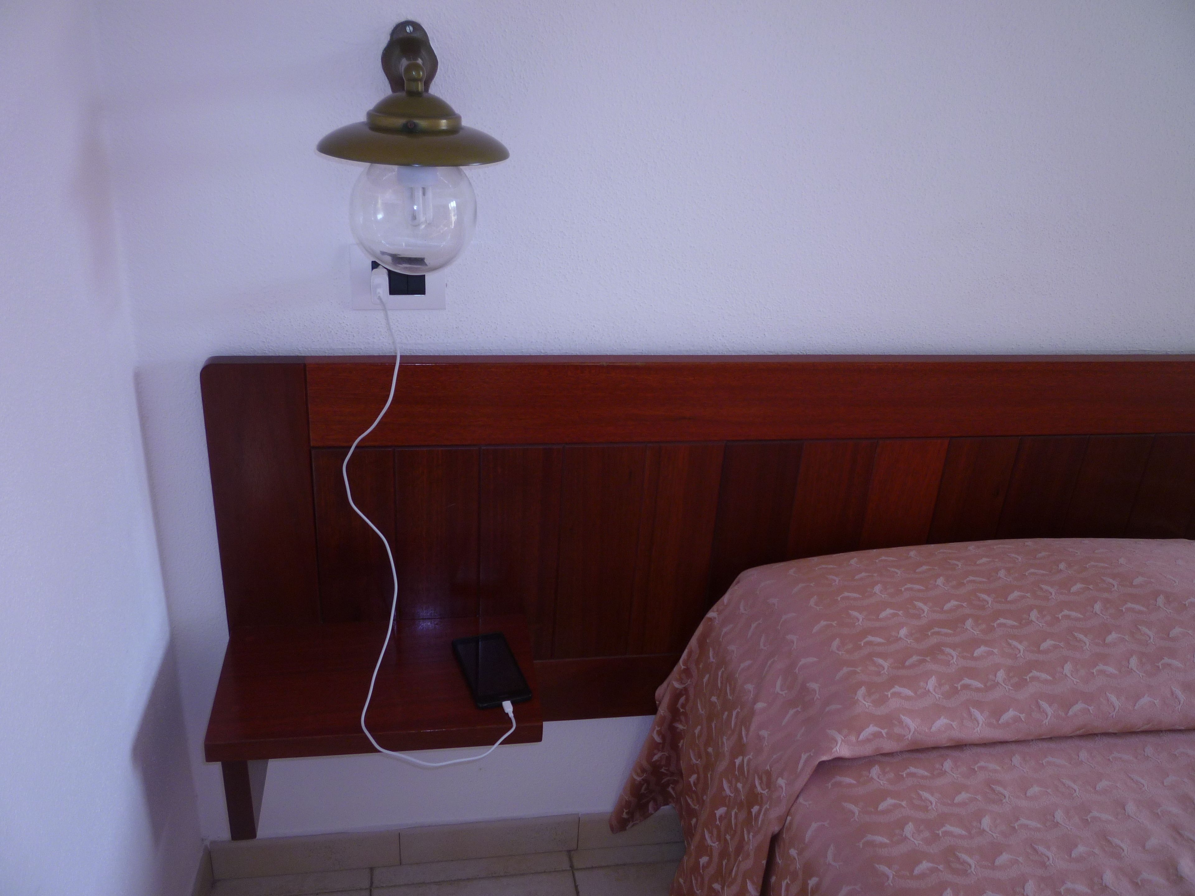 Ein Schlafzimmer mit Holz-Kopfteil, Nachttisch, Lampe und einem Bett mit gemustertem Überwurf.