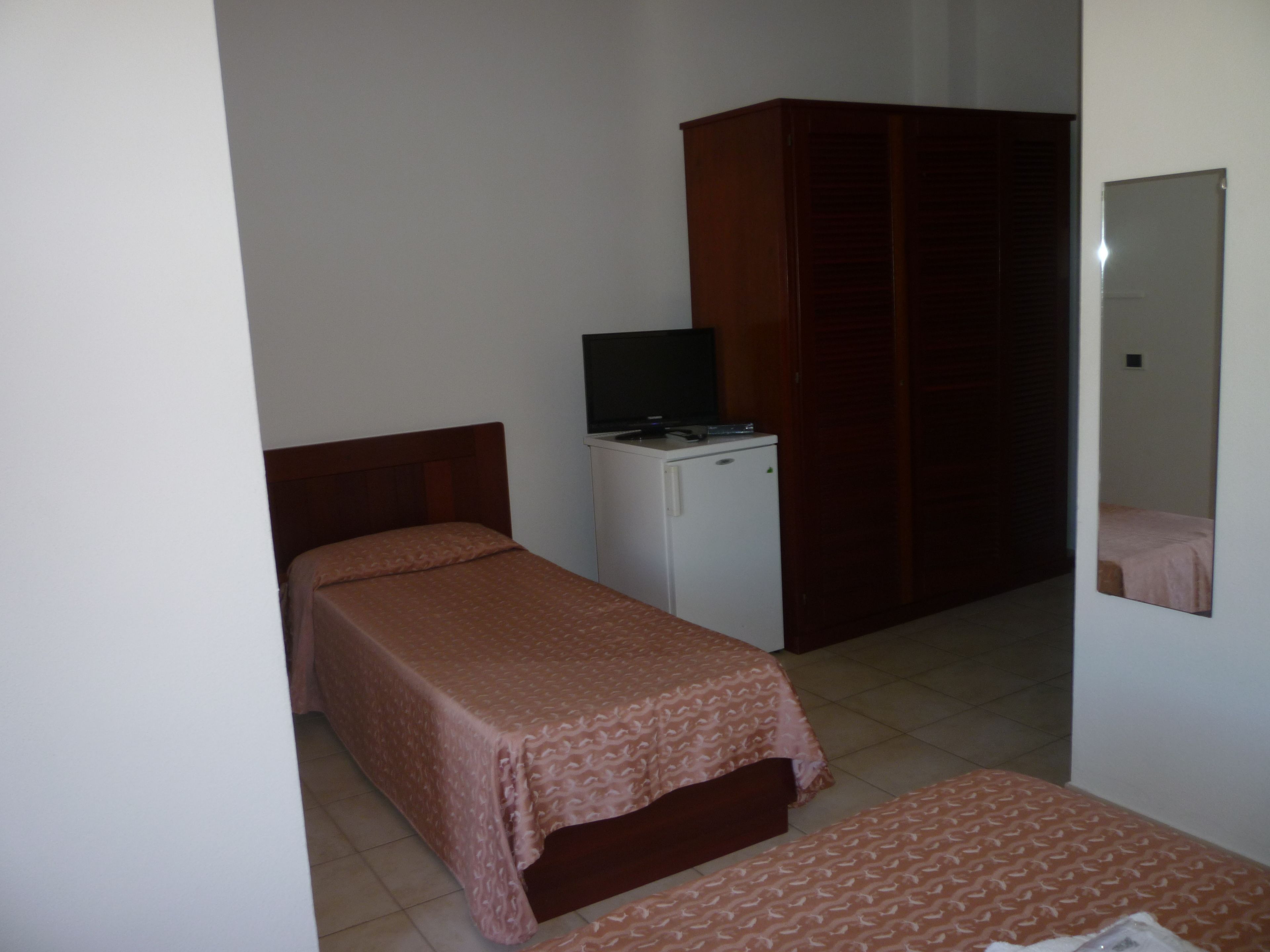 Een kleine, eenvoudige kamer met een bed, een televisie op een kastje, en een kledingkast.