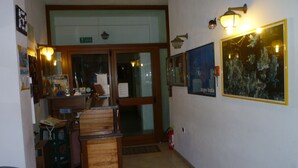 Un hall con mostrador de recepción, una silla, un extintor y lámparas fijadas a la pared.