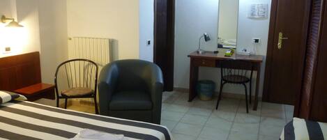 Una habitación de hotel con cama, dos sillas, escritorio, espejo y radiador.