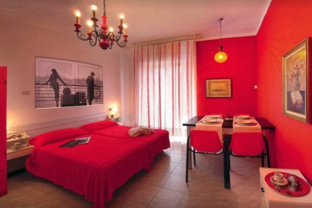 A red-themed bedroom with a bed, bedside tables, a desk, and a chair.