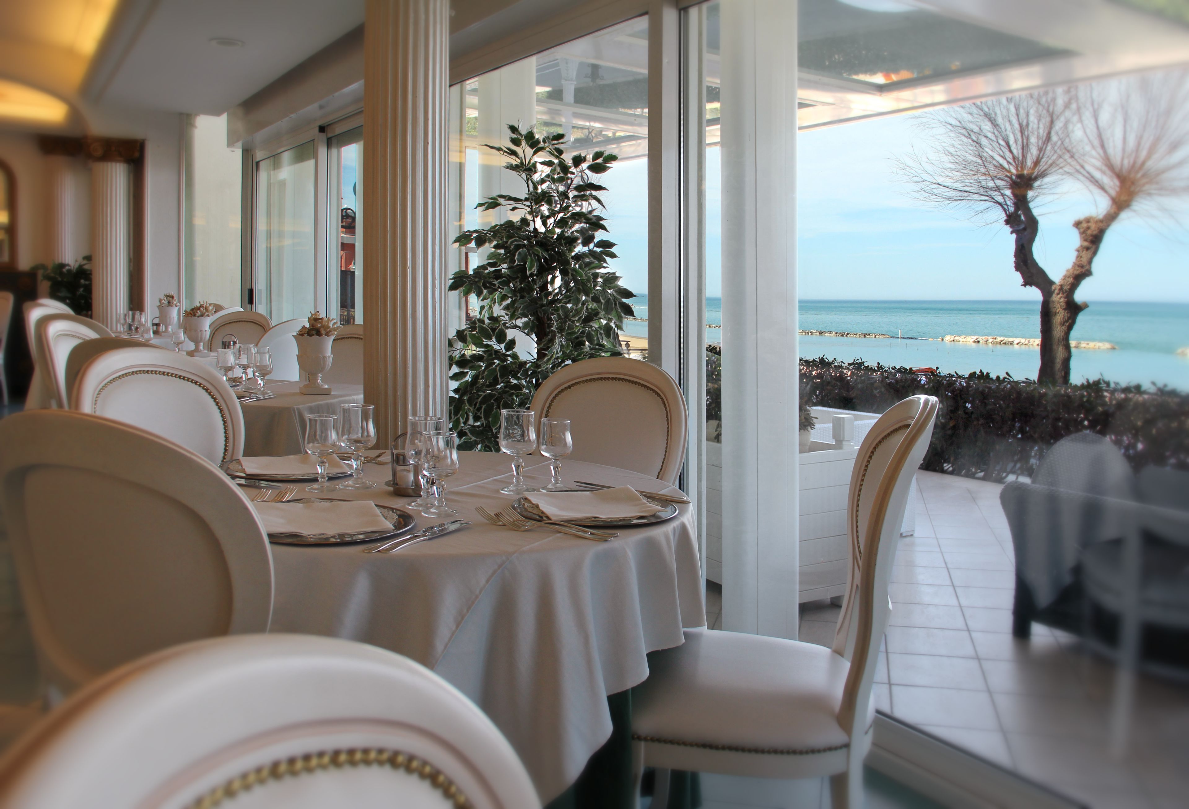 Un ristorante con vista sul mare, caratterizzato da tavoli imbanditi con tovaglie bianche e posateria.